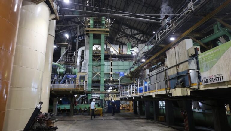 Busy production hall inside a Mauritius sugar mill with a large machine crushing sugarcane and workers present