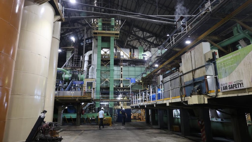 Busy production hall inside a Mauritius sugar mill with a large machine crushing sugarcane and workers present