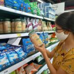 A consumer inspecting packaged organic and refined sugar on a supermarket shelf in Vietnam, illustrating the domestic market oversupply and competition.