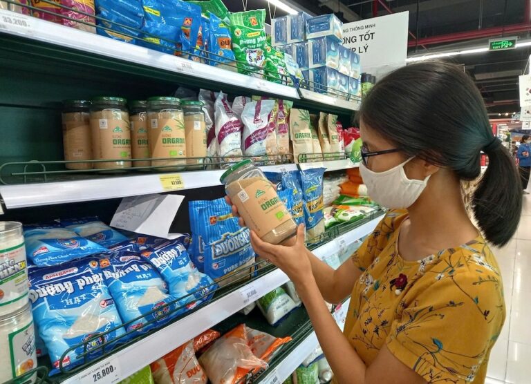 A consumer inspecting packaged organic and refined sugar on a supermarket shelf in Vietnam, illustrating the domestic market oversupply and competition.